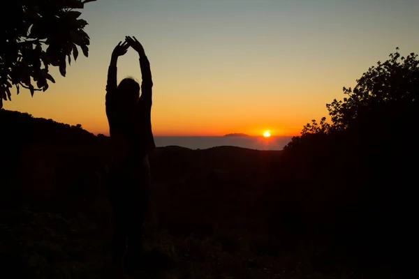 Güneşe bakan genç bir kızın silueti. Elleri havada, muhteşem günbatımının arka planında duruyor.