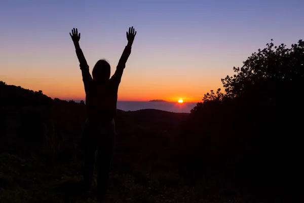 Güneşe bakan genç bir kızın silueti. Elleri havada, muhteşem günbatımının arka planında duruyor.