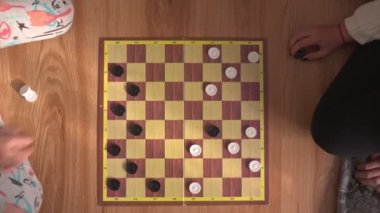 Küçük çocuklar tahta zeminde beraber dama oynuyorlar.