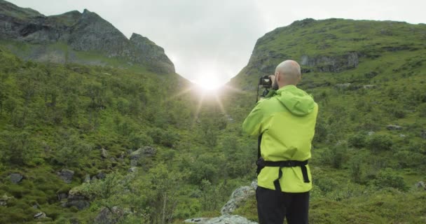 自然摄影师 带着相机和三脚架 站在山丘旁边拍摄太阳耀斑 多云的天气下美丽的挪威罗浮敦群岛 — 图库视频影像