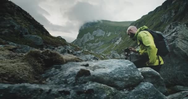 自然摄影师带着相机和三脚架在Kvalvika海滩旁边的岩石地形地区拍摄 多云的天气下美丽的挪威罗浮敦群岛 — 图库视频影像