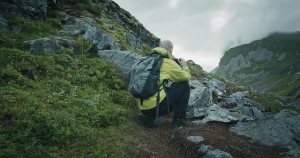 自然摄影师带着相机和三脚架在Kvalvika海滩旁边的岩石地形地区拍摄 多云的天气下美丽的挪威罗浮敦群岛 — 图库视频影像
