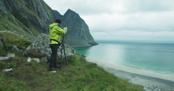 站在Kvalvika海滩旁边时 自然摄影师带着相机和三脚架拍摄 多云的天气下美丽的挪威罗浮敦群岛 — 图库视频影像