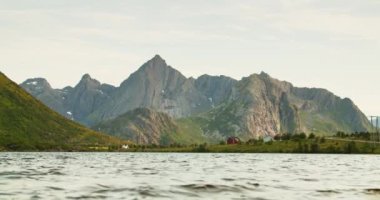 Güneşli bir günde göl ve dağların alçak açılı manzarası. Ön planda su dokuması var. Lofoten Adaları, Norveç fiyortlarının güzel doğası..