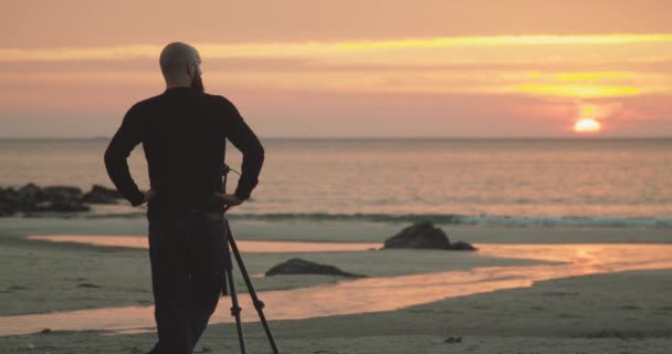 自然摄影师带着相机和三脚架 站在天堂的海滩边 给美丽的落日拍照 — 图库视频影像