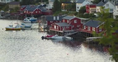 Geleneksel kırmızı kulübeler veya Reine-Lofoten Adaları 'ndaki göl kenarındaki balıkçı kulübeleri. Sabahın erken saatlerinde, bulutlu bir günde. Kıyıya demirlemiş tekneler