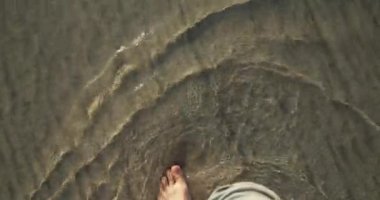 Beyaz kumsal boyunca yürürken, kristal berrak okyanus suyuyla yıkanan çıplak ayaklarınıza bakın. Tropikal kumlu sahilde yürüyen bir adamı ilk gören kişi. Yavaş çekim.