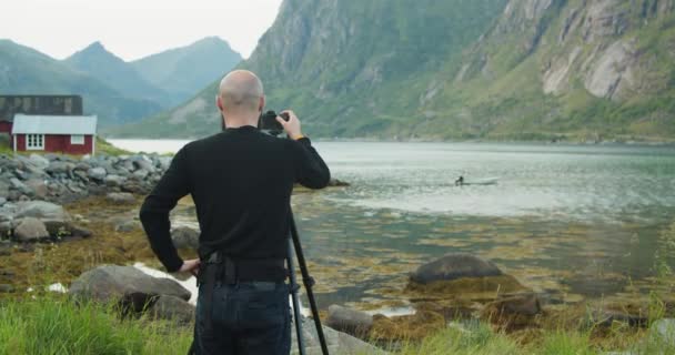 带着相机和三脚架的自然摄影师游客带着一艘船和传统的红色小屋 拍摄了一个挪威湖泊的照片 — 图库视频影像