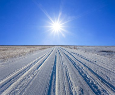 Işıl ışıl güneş ışığında karla kaplı çayırların arasındaki yol, kış yolculuğu arka planı.