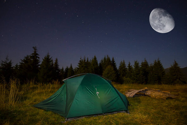 green touristic tent stay on forest glade at the night