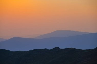 Dağ silueti mavi sisli gün batımında, sabahın erken saatlerinde dağ yolculuğu sahnesi