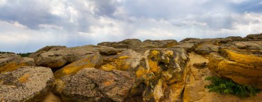 heap of huge stones lie on sandy hill under dense cloudy sky, wild sandy desert landscape