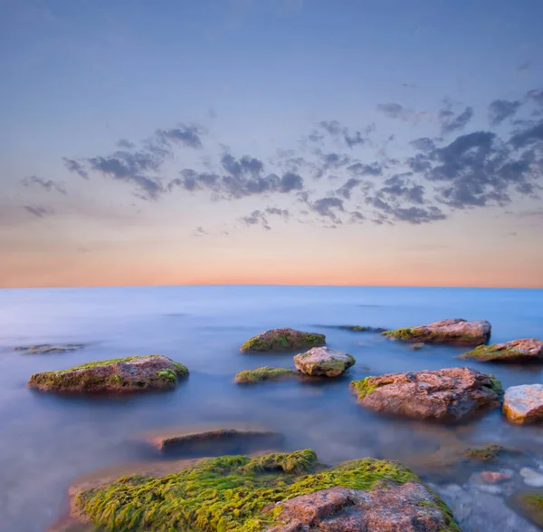 夕暮れ時の長い露出の海のシーンで石のヒープと海の海岸 — ストック写真