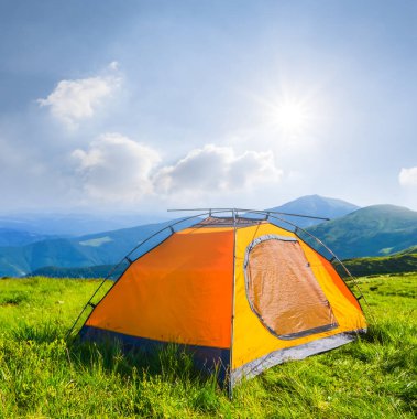 Kapalı turuncu turistik çadır güneşli bir günde yeşil dağda kalır, dağ yolculuğu sahnesi