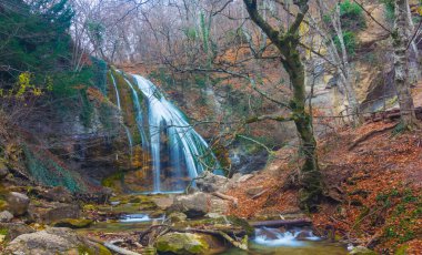 Zümrüt nehri üzerindeki güzel şelale dağ kanyonu boyunca akar kırmızı kuru yapraklarla kaplıdır, sonbahar nehri manzarası.