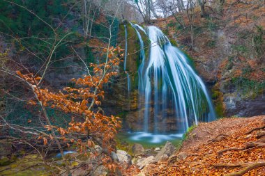 Zümrüt nehri üzerindeki güzel şelale dağ kanyonu boyunca akar kırmızı kuru yapraklarla kaplıdır, sonbahar nehri manzarası.