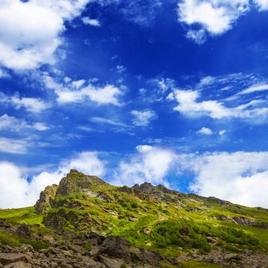 Mavi bulutlu gökyüzünün altındaki yeşil dağ sırtı