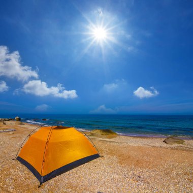 Turuncu turistik çadır güneşli bir günde kumlu deniz sahilinde kalır.