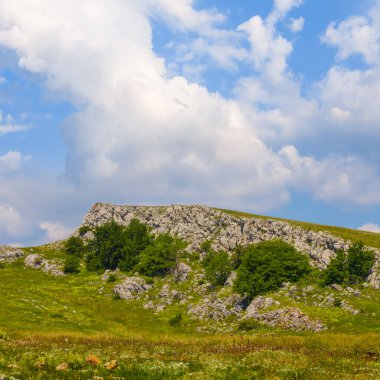 Mavi bulutlu gökyüzünün altındaki yeşil tepelerin arasındaki dağ sırtı