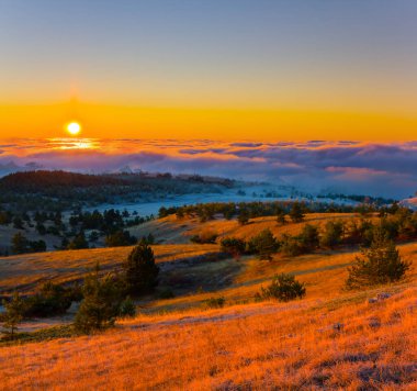 Yoğun sisli dağ vadisi ve gün batımında bulutlar