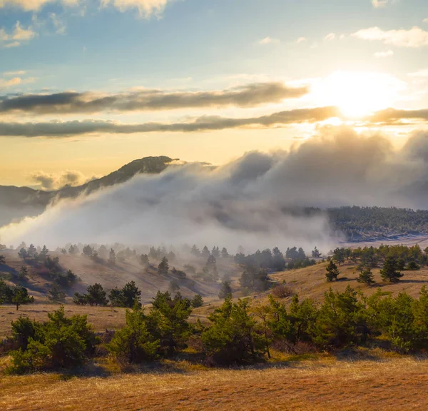 Yoğun sisli dağ vadisi ve gün batımında bulutlar