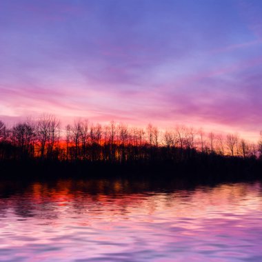 Göl kıyısındaki orman silueti alacakaranlıktaki suya yansıyor. 