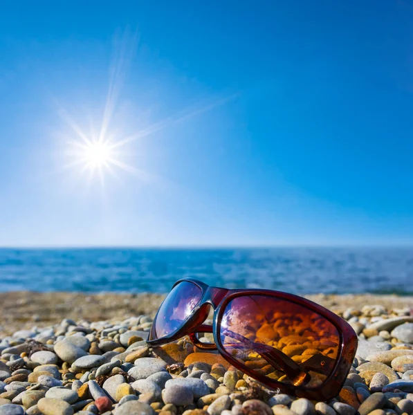 closeup sunglasses lie on a stony sea coast in light of sparkle sun, summer sea vacation background