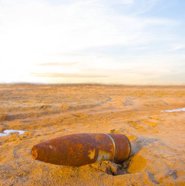 Paslı eski bomba kumlu çayırda günbatımında yatıyor.