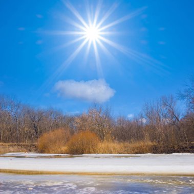 Güneşli kış gününde karla kaplı donmuş nehir, parlak mevsimlik manzara.