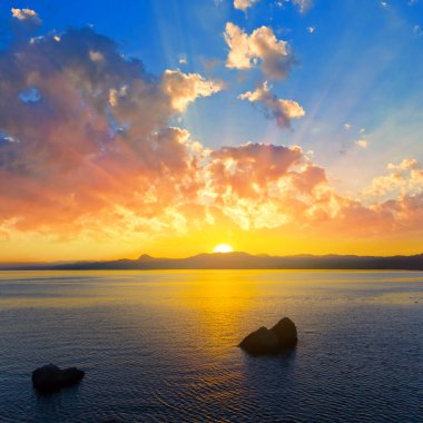 Gün batımında taş siluetiyle sakin bir deniz koyunda