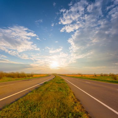 Uzun asfalt yolu gün batımında uzaklaşıyor.