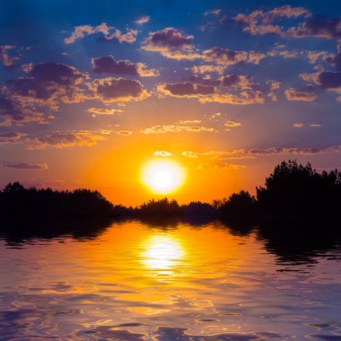 Dramatik günbatımı sakin göle yansıyor. Sahilde orman silueti.