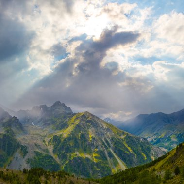 Işıl ışıl güneşin altında yoğun bulutlarda karlı dağ zinciri
