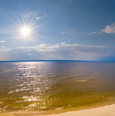 Parlak güneşin altında kumlu kıyıları olan geniş bir göl.