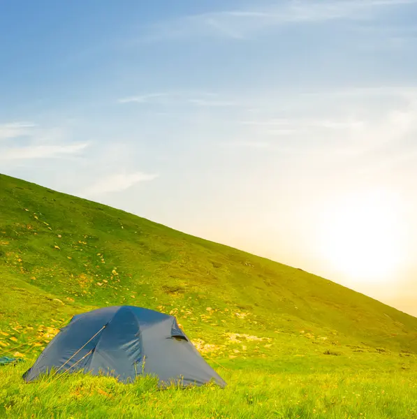 Güneş batarken yeşil dağ yamacına yakın turistik çadır, yaz tatili manzarası.
