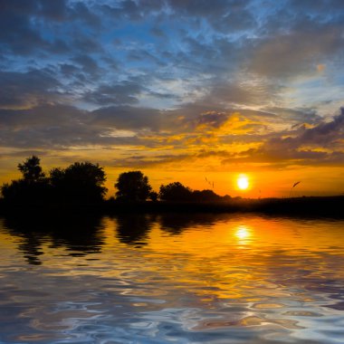 Sakin göl dramatik günbatımı bir suya yansıyor.