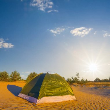 Küçük yeşil turistik çadır gün batımında kumlu çölde kalır.