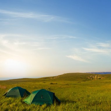 Gün batımında bir çift yeşil turistik çadır, akşam kampı sahnesi