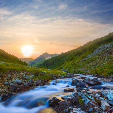 Gün batımında dağ vadisinde küçük bir dere.