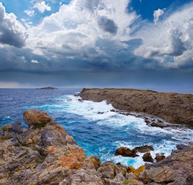 Yoğun bulutlu gökyüzü altında kayalık kıyıları olan fırtınalı deniz koyuna. 