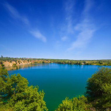Bulutlu bir gökyüzünün altında kayalık kıyıları olan zümrüt göl