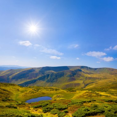 Parlak güneşin altında, yeşil dağın arasında küçük bir göl.