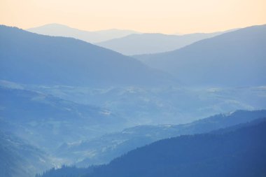 Bulutlu gökyüzünün altında yoğun siste yeşil dağ zinciri