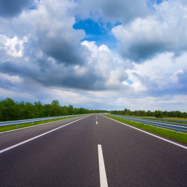 Yoğun bulutlu bir gökyüzünün altında uzun asfalt yol