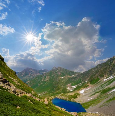 Işıldayan güneşin altında küçük mavi gölü olan yeşil dağ vadisi