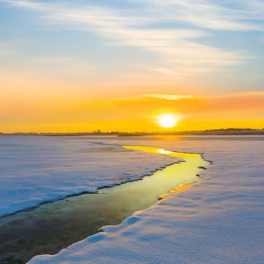 Gün batımında karla kaplı küçük bir dere.