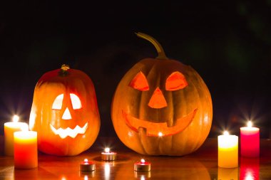 Bir çift cadılar bayramı balkabağı yanan mum arasında, karanlıkta bir masada.