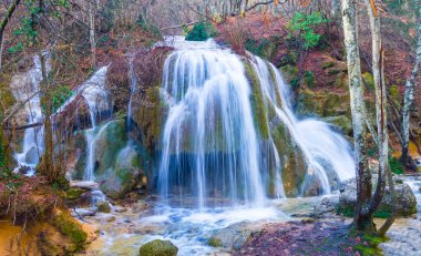 Küçük dağ nehrindeki şelale kırmızı kuru yapraklarla kaplı kanyon boyunca akıyor.