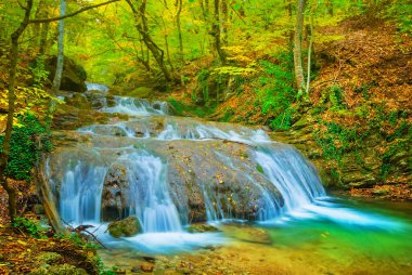 Küçük dağ nehrindeki şelale kırmızı kuru yapraklarla kaplı kanyon boyunca akıyor.