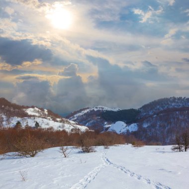 Karlı, sisli dağ vadisi, güneş ışığı, kış dağı manzarası.